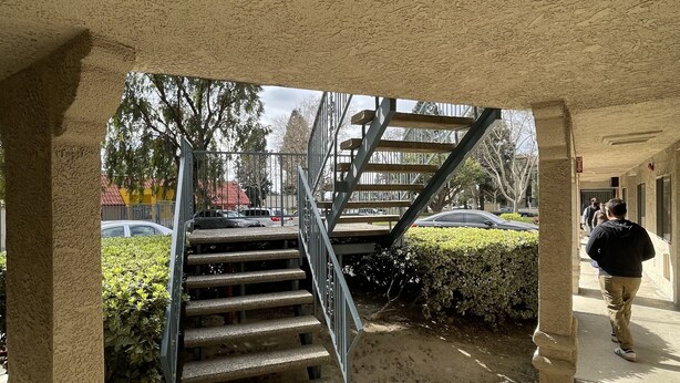 Eine Betontreppe führt zu einer erh öhten Ebene, umgeben von Steinsäulen und einem überdachten Gang.