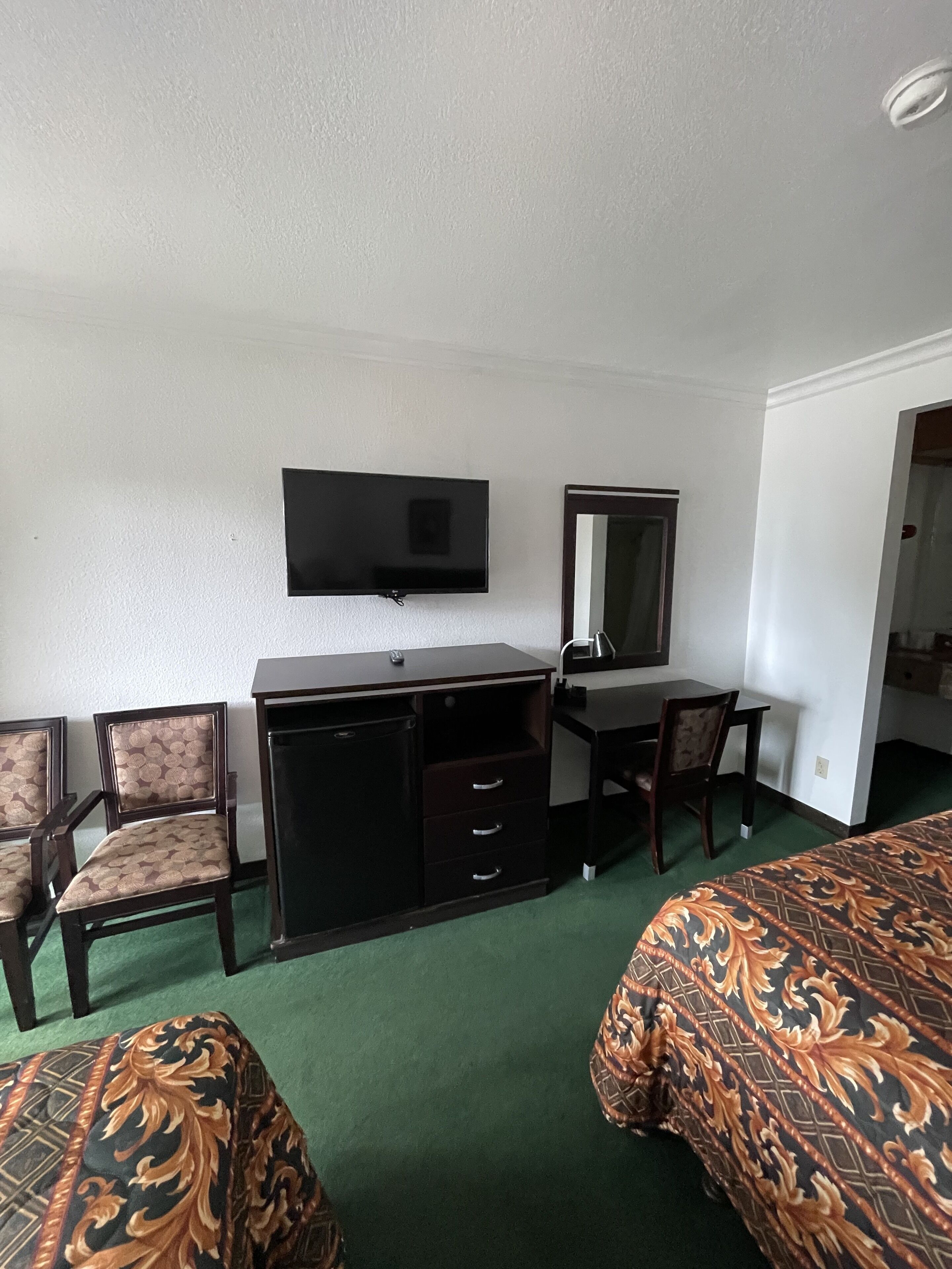 A hotel room with a bed, a desk with a chair, a television, and a mirror.