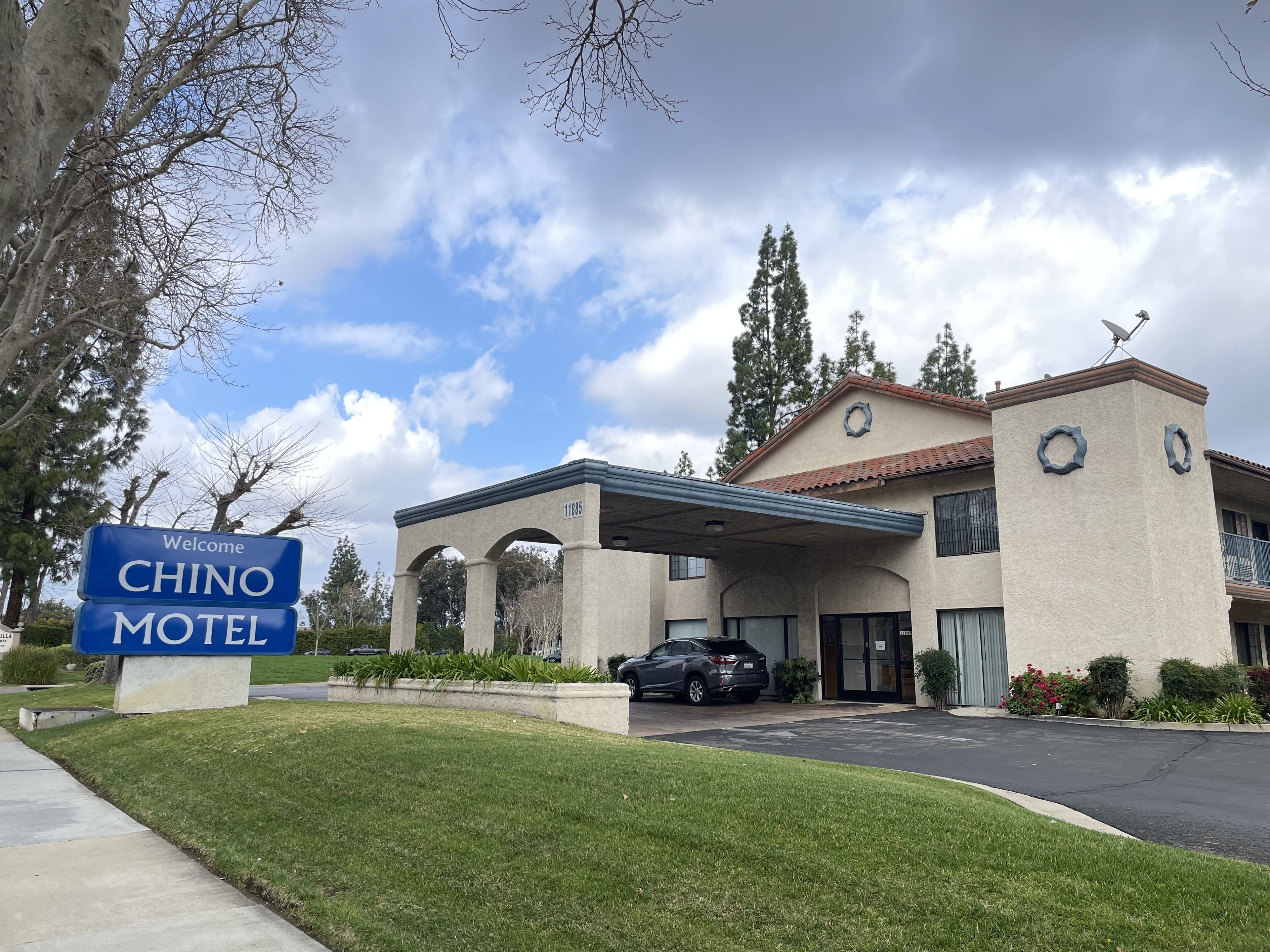 A CHINO motel with a covered entrance, a parking lot, and a sign welcoming visitors.