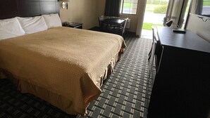 Ein Hotelzimmer mit einem großen Bett, einem Schreibtisch, einem Sessel und einem Fernseher.