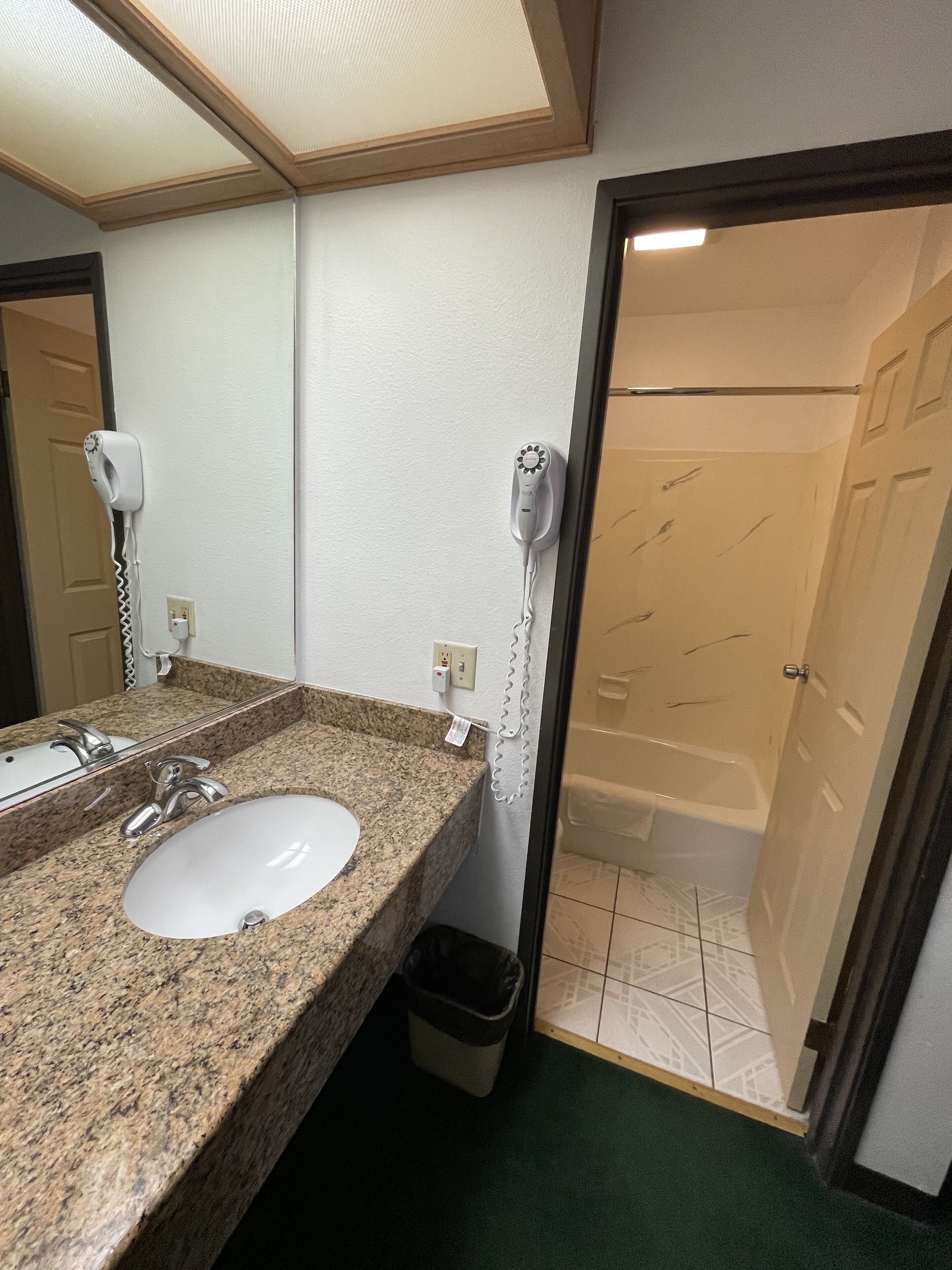 Un baño con lavamanos de granito, un espejo, secador de pelo y cabina de ducha.