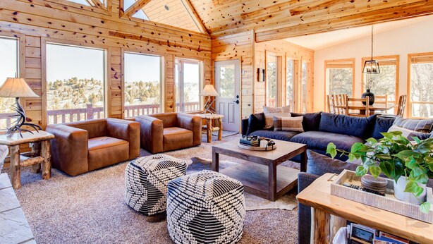 Un vaste salon aux murs en bois et aux grandes fenêtres, aménagé avec des canapés en cuir, des poufs et une table basse.
