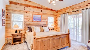 Une chambre dans une cabane en bois, avec un lit, des tables de chevet, un ventilateur de plafond et de grandes fenêtres.