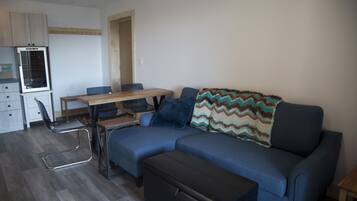 Una sala de estar moderna con un sofá azul, una mesa de comedor de madera y una zona de cocina con refrigerador.