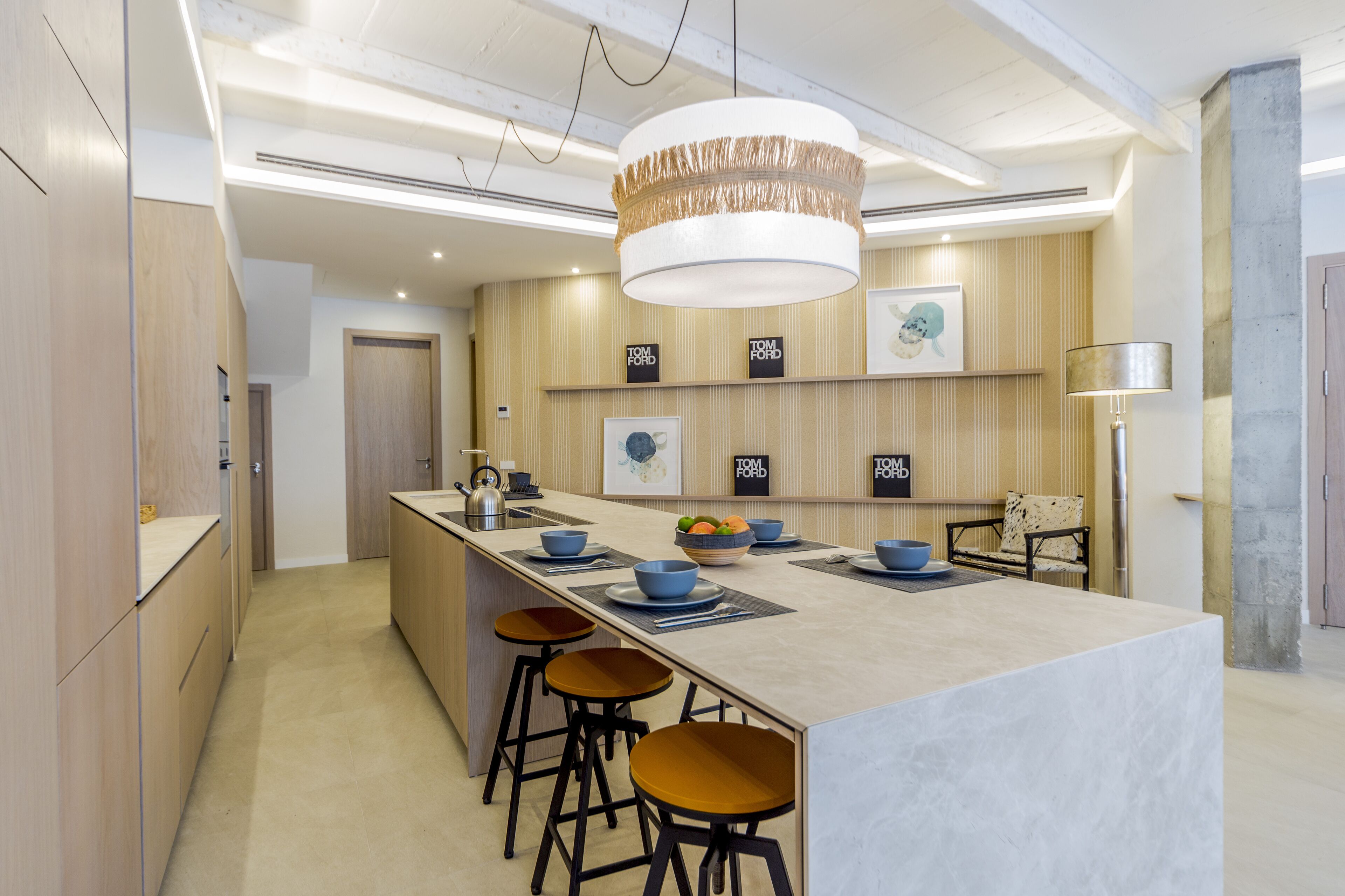 A modern kitchen with a central island, bar stools, and a hanging light fixture.