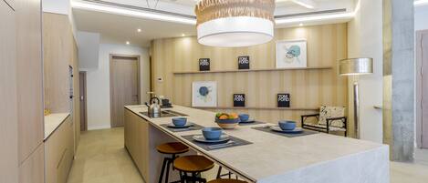 A modern kitchen with a central island, bar stools, and a hanging light fixture.
