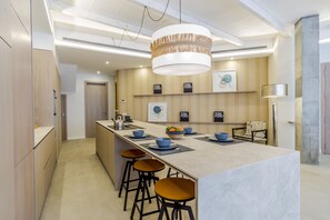 A modern kitchen with a central island, bar stools, and a hanging light fixture.