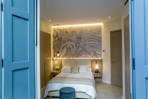 A modern bedroom with a large bed, a headboard with a leaf pattern, bedside lamps, and a nightstand.