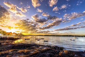Cena à beira-mar com barcos, costa rochosa e um pôr do sol.