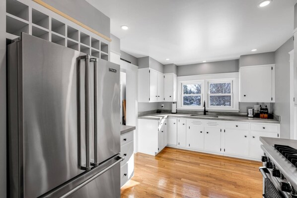 A modern kitchen with white cabinets, a stainless steel refrigerator, and wooden flooring. - Rye Retreat (Rye)