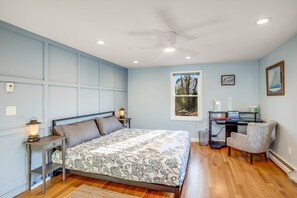 A bedroom with a bed, a desk, a chair, a ceiling fan, and a window with a view of trees. - Blue Hour (Marblehead)