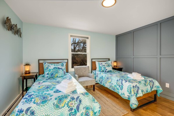 Une chambre avec deux lits, une fenêtre et une vue sur les arbres à l’extérieur.
