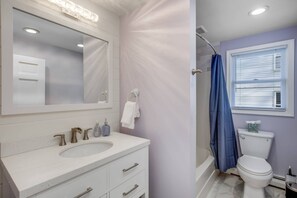 A bathroom with a white sink, mirror, and vanity, a toilet, and a shower with a blue curtain. - Blue Hour (Marblehead)