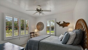 Un dormitorio con cama, ventilador de techo y dos ventanas con contraventanas.