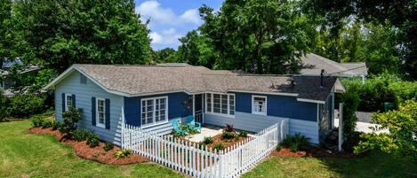 A single-story house with a white picket fence, a front porch, and a small garden area.