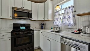 Una cocina moderna con gabinetes blancos, microondas integrado, estufa, fregadero y lavavajillas.