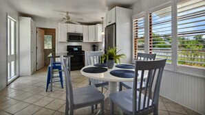 Una cocina con armarios blancos, un microondas y un refrigerador. Hay una mesa de comedor con sillas y una planta en maceta.