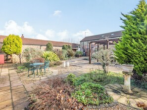 Ein Garten mit einer Pergola, einer Steinsitzbank und verschiedenen Pflanzen.