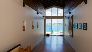 A hallway with wooden floors, a bench, and a view of the sea through large glass doors.