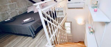 A bedroom with a bed, a staircase, a stone wall, and a small window.