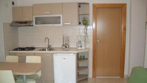 Cocina compacta con refrigerador, estufa, microondas, lavaplatos y un pequeño comedor con mesa y sillas.