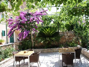 Eine Terrasse im Freien mit Korbmöbeln, einer Steinmauer und purpurfarbenen Bougainvillea-Blüten.