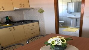 A small kitchen with a stove, sink, and cabinets. There is a dining table with a vase of flowers.
