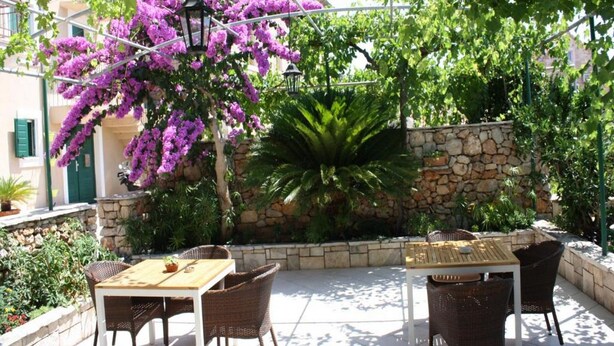 An outdoor patio with wicker furniture, a stone wall, and purple bougainvillea flowers.