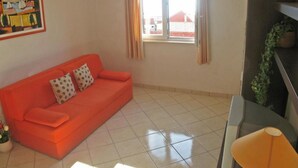 Una habitación con un sofá rojo, una mesita, una ventana con cortinas y un cuadro en la pared.