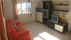 Un espacio habitable pequeño con sofá, televisor, armarios y ventana con cortinas.