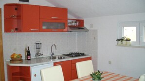 Una cocina compacta con armarios rojos, un fregadero y un pequeño comedor con mantel a cuadros.