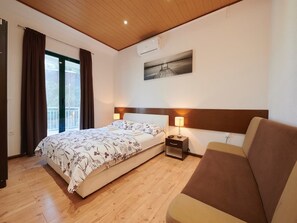 Una camera d'albergo con un letto, un comodino, una lampada, un divano, una finestra con tende e un quadro appeso al muro.