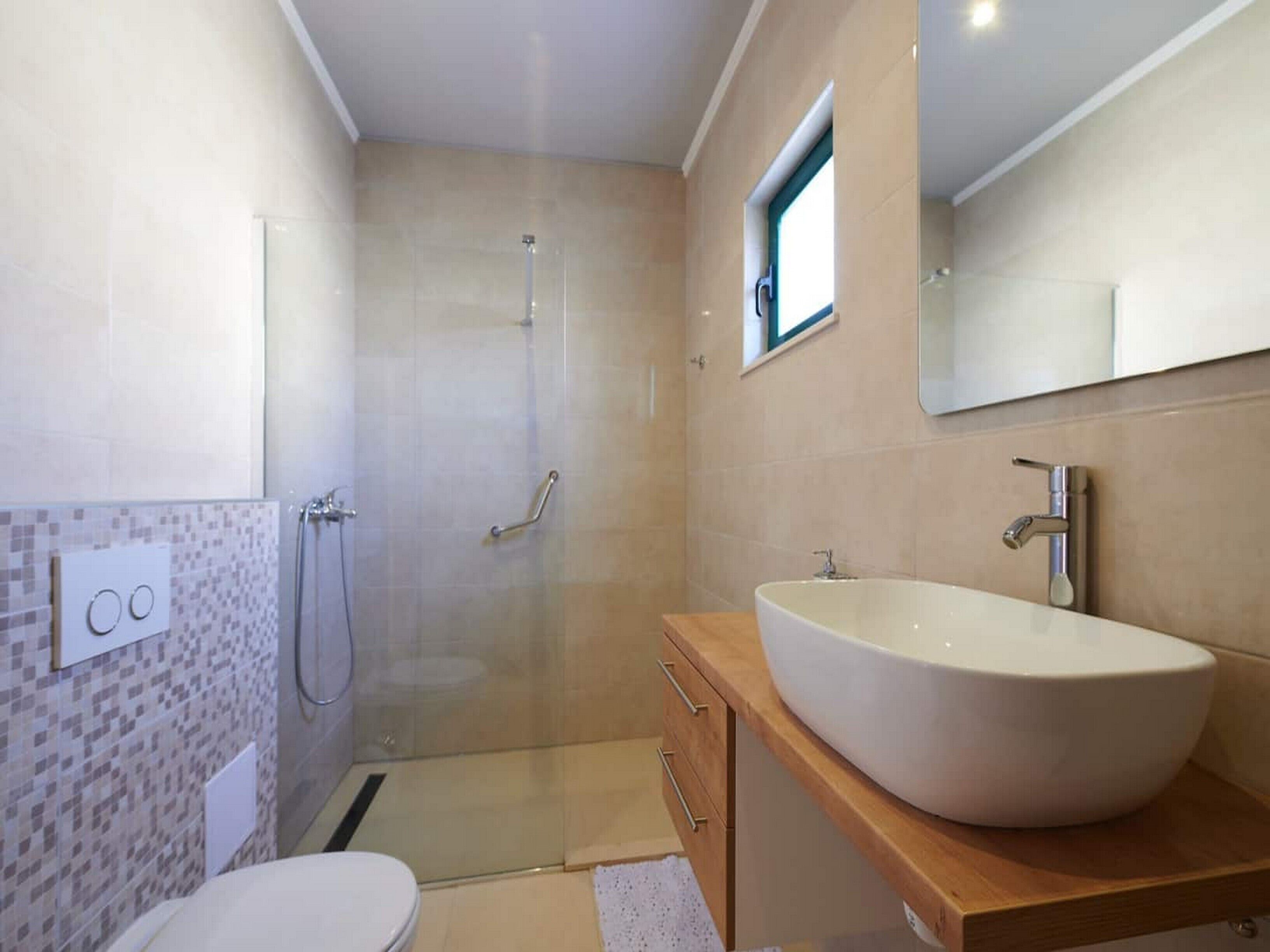 Une salle de bain moderne avec un grand lavabo blanc, une cabine de douche en verre et une petite fenêtre au-dessus du miroir.