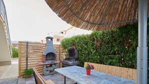 An outdoor patio with a wooden table, a bench, a barbecue grill, and a pizza oven. - Apartments Vujina - Studio 3 (Kastel Stafilic)