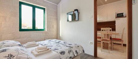 A bedroom with a bed, a window, a television, and a view of a dining area.