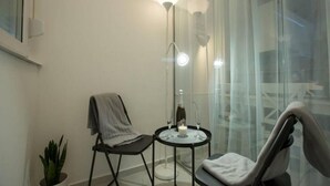 Een kleine, moderne kamer met een glazen scheidingswand, een tafeltje met een kaars, een stoel en een potplant.