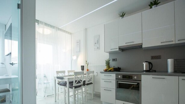 Een moderne keuken met witte kasten, een eethoek met een glazen tafel en uitzicht op de omgeving.