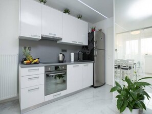 A modern kitchen with white cabinets, stainless steel appliances, and a dining area with a table and chairs. - Modern & Luxury APT Zagreb Airport W/ free WiFi - One Bedroom Apartment (Velika Gorica)