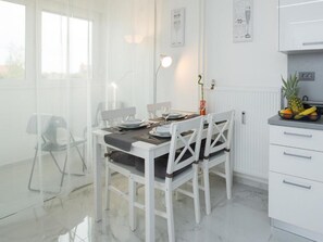 A modern kitchen with white cabinetry, a dining table set for four, and a fruit bowl on the counter. - Modern & Luxury APT Zagreb Airport W/ free WiFi - One Bedroom Apartment (Velika Gorica)