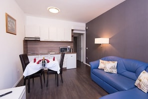 Een knus woongedeelte met een eethoek, kitchenette en een blauwe bank.