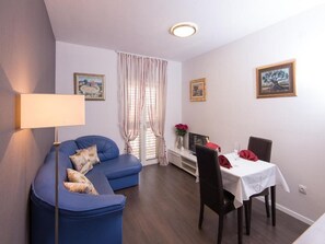 A living room with a blue sofa, a dining table with chairs, and a lamp.