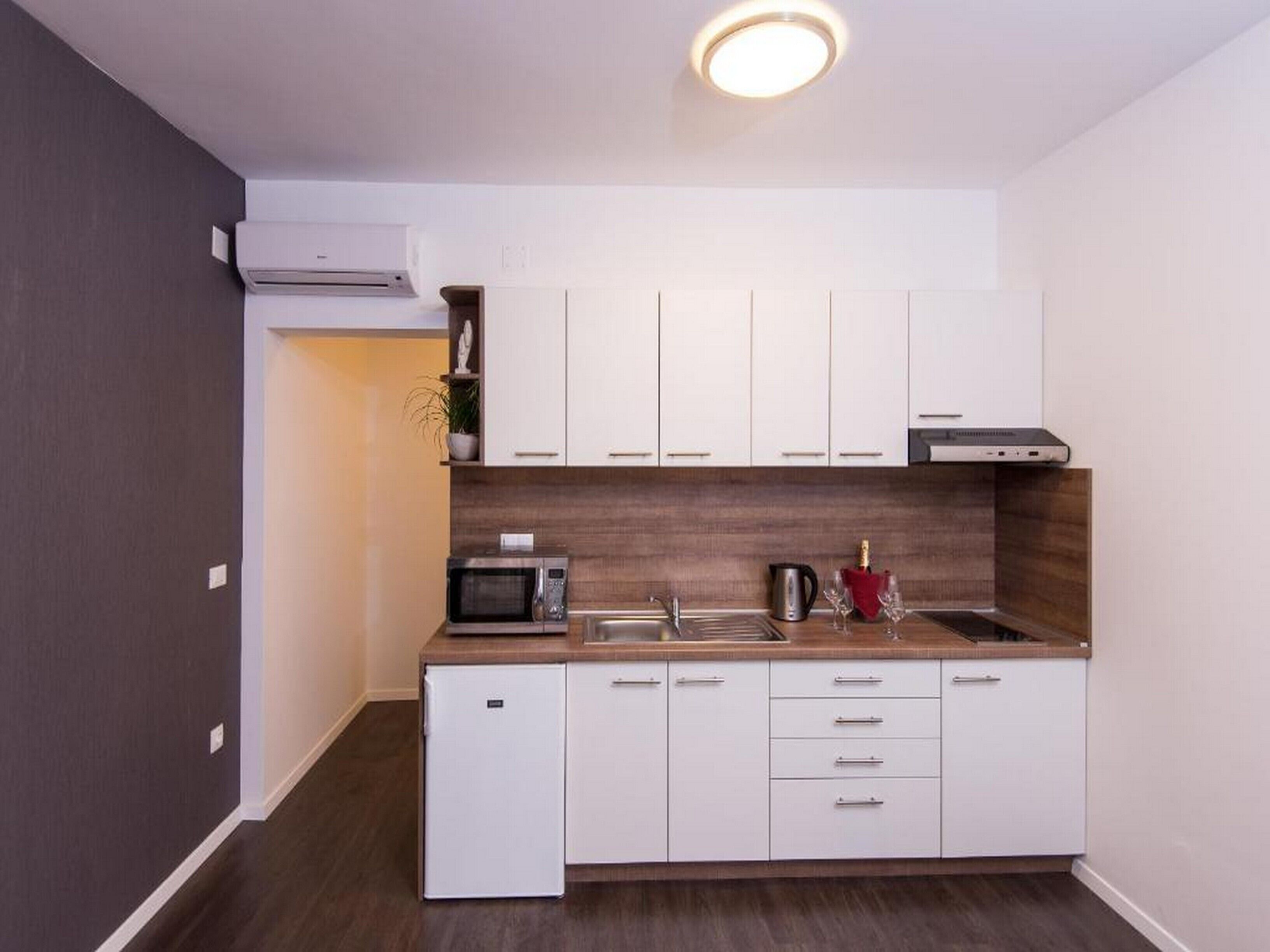 A compact kitchen with white cabinets, a microwave, a sink, and a small refrigerator.