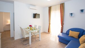 Ein modernes Wohnzimmer mit einem blauen Sofa, einem Esstisch mit Stühlen und einem an der Wand befestigten Fernseher.