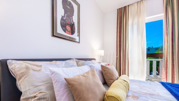 Ein Hotelzimmer mit einem Bett, Kissen, einem gerahmten Bild an der Wand und Blick ins Freie.