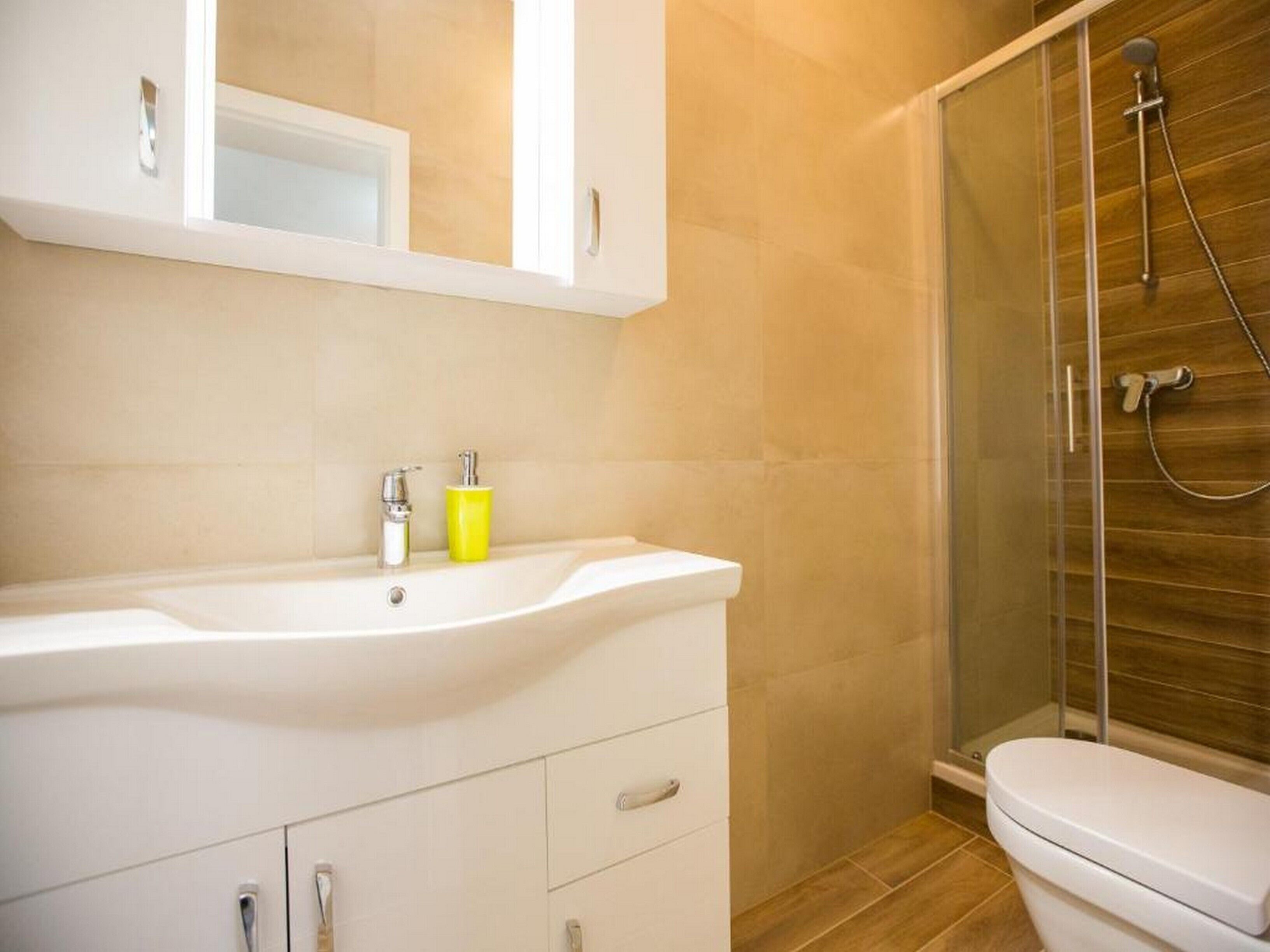 A bathroom with a white sink, yellow soap dispenser, and a glass shower enclosure.