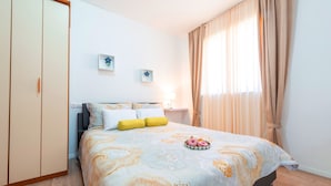 Un dormitorio con cama, cortinas, mesita de noche y adornos en la pared.