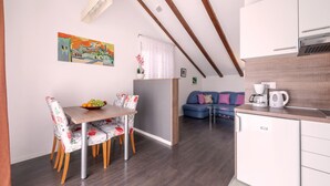 Une cuisine moderne dotée d’un four encastré, un coin repas avec une table en bois et des chaises à motifs floraux, et un salon avec un canapé et des coussins.