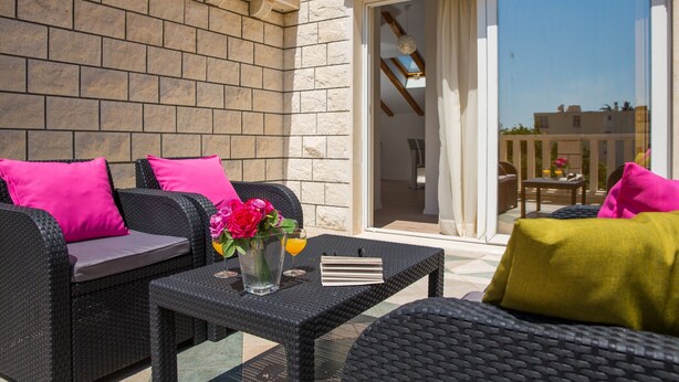 Une terrasse extérieure aménagée avec des meubles en osier, une table ornée d’un vase de fleurs et une porte-fenêtre coulissante donnant sur un espace intérieur.