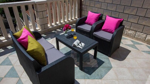 Eine Terrasse mit Korbmöbeln, darunter zwei Sofas und ein Tisch, sowie eine dekorative Vase mit Blumen.