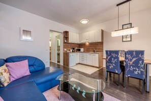 A modern living room with a blue sofa, a glass coffee table, and a dining area with blue chairs.
